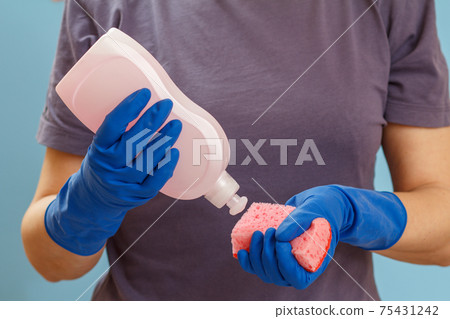 Woman holding a bottle of dishwashing liquid and a sponge on a blue background. 75431242