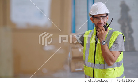 Professional cargo worker talks on portable radio to contact another worker Professional cargo worker talks on portable radio to contact another worker 75431650