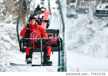 Skier sitting at ski lift talking on the phone in high mountains during sunny day. Winter sport and recreation, leisure outdoor activities. Skier sitting at ski lift talking on the phone in high mountains during sunny day. Winter sport and recreation, leisure outdoor activities. 75431738
