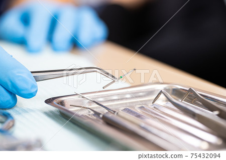 Dental instruments close up. the dentist holds a drill for a power drill with tweezers. Dental treatment. 75432094