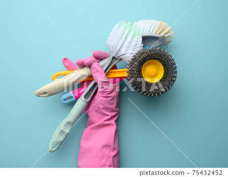 female hand in a pink glove holds a stack of plastic cleaning brushes 75432452