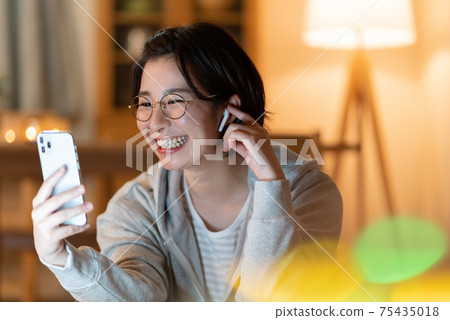 一個年輕的女人在晚上在客廳裡在她的智能手機上進行變焦對話 75435018