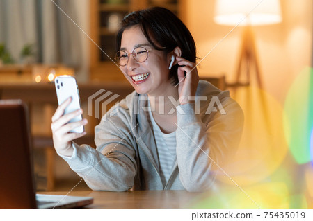 A young woman having a zoom conversation on her smartphone in the living room at night A young woman having a zoom conversation on her smartphone in the living room at night 75435019