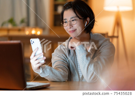 一個年輕的女人在晚上在客廳裡在她的智能手機上進行變焦對話 75435028