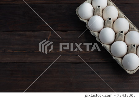 Fresh chicken eggs in a package, raw eggs in a white shell in a box. Top view copy space, wooden background. 75435303