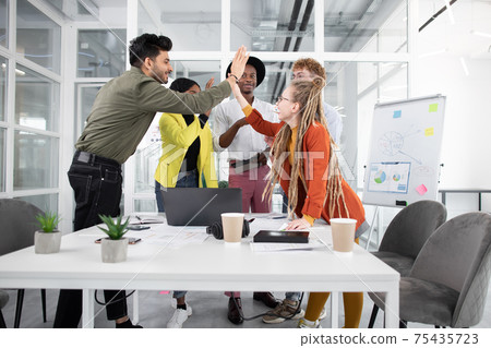 Mixed race people giving high five after successful meeting in modern office Mixed race people giving high five after successful meeting in modern office 75435723