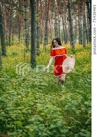 Enjoying the nature, wellness, wellbeing, healthy lifestyle, slow living. Young brunette girl in red dress and straw hat walking in forest, woods. 75436465