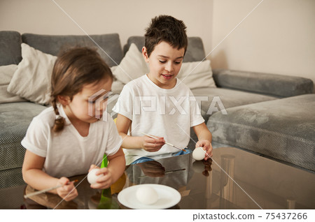 Two adorable children holding eggs and paintbrushes ready for coloring Easter eggs. 75437266