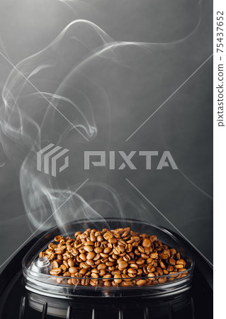 fresh roasted coffee beans with smoke in coffeemaker bean container, close-up view 75437652