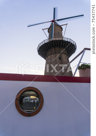 Twilight after sunset shot Of Highest Windmill in the World and Vessel on Foreground in Schiedam, Netherlands is famous for its windmills and also Jenever, a type of gin Twilight after sunset shot Of Highest Windmill in the World and Vessel on Foreground in Schiedam, Netherlands is famous for its windmills and also Jenever, a type of gin 75437741