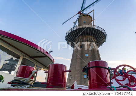 Twilight after sunset shot Of Highest Windmill in the World and Vessel on Foreground in Schiedam, Netherlands is famous for its windmills and also Jenever, a type of gin Twilight after sunset shot Of Highest Windmill in the World and Vessel on Foreground in Schiedam, Netherlands is famous for its windmills and also Jenever, a type of gin 75437742
