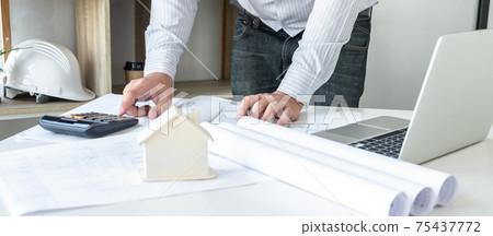 Architects or engineering working on objects tools and construction planning new architectural project on blueprint and model house in modern office Architects or engineering working on objects tools and construction planning new architectural project on blueprint and model house in modern office 75437772