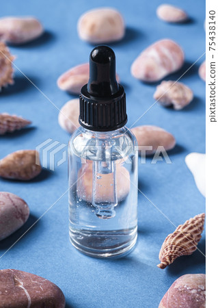 Skin care essence oil dropper in glass bottle near to seashells and pebbles 75438140