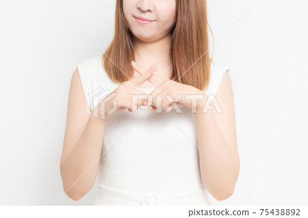 Young woman standing in front of a white wall and making an NG gesture Young woman standing in front of a white wall and making an NG gesture 75438892