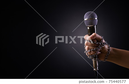 World press freedom day concept. Hand holding a microphone with chain on dark background, symbol of press freedom of speech freedom. World press freedom day concept. Hand holding a microphone with chain on dark background, symbol of press freedom of speech freedom. 75440577