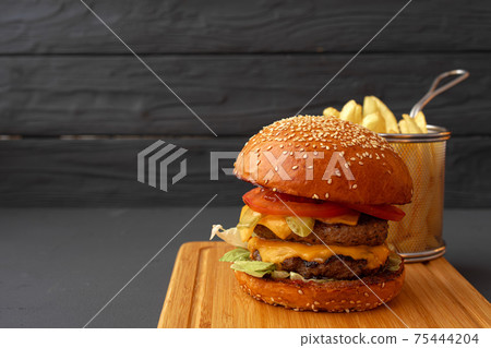 Delicious burger and fries on wooden board against black background Delicious burger and fries on wooden board against black background 75444204