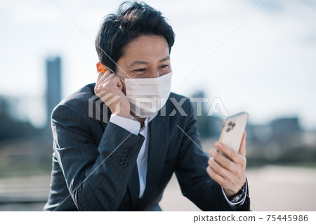 A businessman wearing a mask looking at a smartphone 75445986