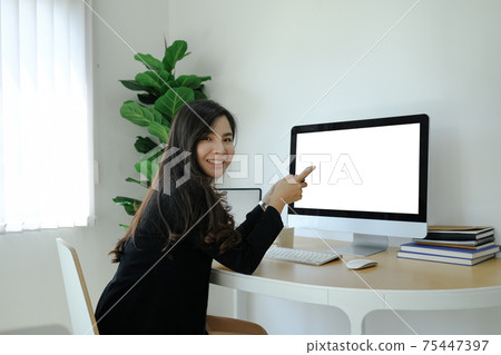Side view of happy businesswoman holding mobile phone and smiling to camera while sitting in front of computer at workplace. Side view of happy businesswoman holding mobile phone and smiling to camera while sitting in front of computer at workplace. 75447397