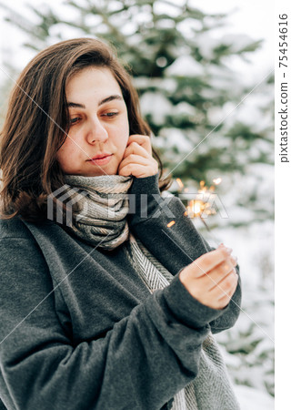Adult young woman with sparklers on the background of winter pine forest 75454616