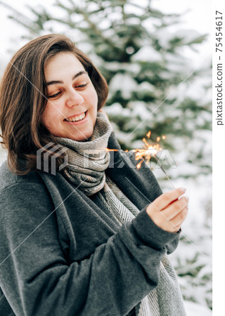 Adult young woman with sparklers on the background of winter pine forest 75454617
