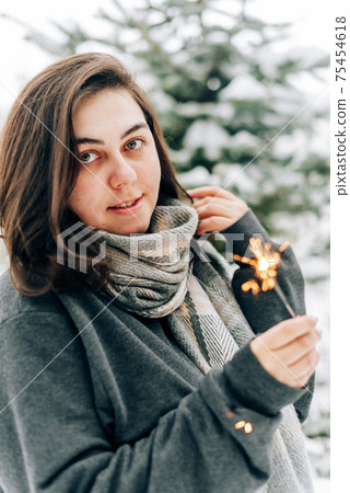 Adult young woman with sparklers on the background of winter pine forest Adult young woman with sparklers on the background of winter pine forest 75454618
