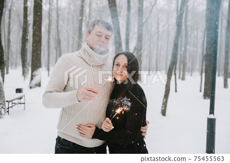 A man and a woman with sparklers on the background of a snow-covered forest in a snowfall 75455563