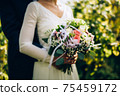 Wedding bouquet composed of roses,other types of flowers,decorative leaves and completed with white ribbon with lace.Bride holding bouquet in hands of groom's victim.Image with shallow depth of field. 75459172