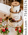 Wedding 3-storey cake that imitates pieces of tree trunk-birch. Cake complemented by natural decorations(cones,branches,flowers). On cake is carved heart pierced by arrow. Focused on center of cake. 75459174
