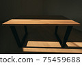 Modern wooden table made of solid wood and angular iron structures in form of legs on sides.Table is in empty room with white wall and wooden floor. Sunlight falls on table and creates contrast scene. 75459688