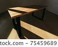 Modern wooden table made of solid wood and angular iron structures in form of legs on sides.Table is in empty room with white wall and wooden floor. Sunlight falls on table and creates contrast scene. 75459689