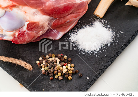 raw pork knuckle with garlic, salt and spices on black stone cutting board. raw pork knuckle with garlic, salt and spices on black stone cutting board. 75460423