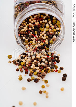 a mixture of peppers is scattered from a jar on a white background. 75460427