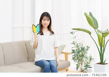 年輕女子坐在沙發上，手裡拿著一個初學者的標記 75462199