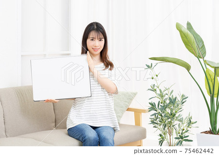 Young woman sitting on the couch and holding a large sketchbook Young woman sitting on the couch and holding a large sketchbook 75462442