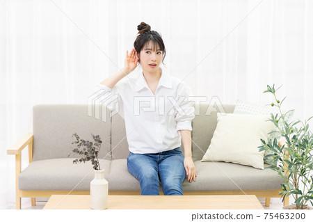 A young woman sitting on a sofa by the window and listening A young woman sitting on a sofa by the window and listening 75463200