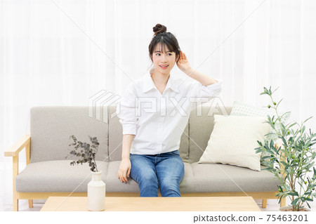 A young woman sitting on a sofa by the window and listening 75463201