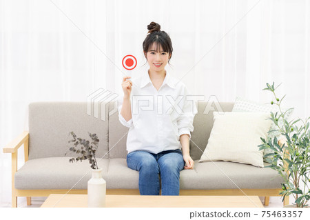 Young woman sitting on the couch by the window and holding an OK placard 75463357