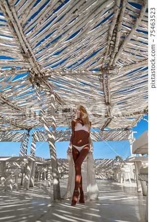 Attractive young woman wearing swimsuit and pareo standing over white bamboo wall Attractive young woman wearing swimsuit and pareo standing over white bamboo wall 75463523
