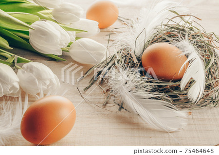 Easter eggs nature. Natural colour egg in basket with spring tulips, white feathers on wooden table background in Happy Easter decoration. Congratulatory easter design. Easter eggs nature. Natural colour egg in basket with spring tulips, white feathers on wooden table background in Happy Easter decoration. Congratulatory easter design. 75464648