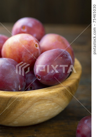 Ripe plums in a wooden bowl on the table. 75465030