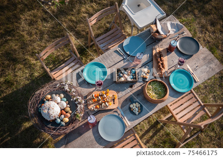Wooden table in the garden, served with dishes and Easter cake 75466175