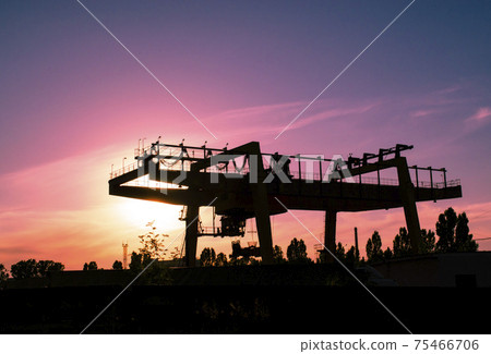 Industrial iron large metal gantry crane mounted on the supports for lifting and carrying heavy cargo, moving along the rails at the factory. The crane is of bridge type. 75466706