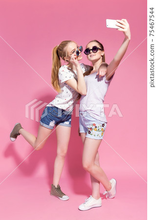 Young happy smiling friends women posing isolated over pink wall background take selfie Young happy smiling friends women posing isolated over pink wall background take selfie 75467544