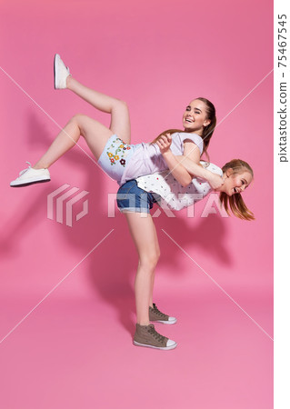 Two cheerful excited young women having fun together over pink background Two cheerful excited young women having fun together over pink background 75467545