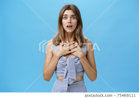 Waist-up shot of woman feeling bad for friend empathizing hearing shocking story gasping opening mouth and looking speechless holding palms on breast standing intense and nervous over blue wall 75469111