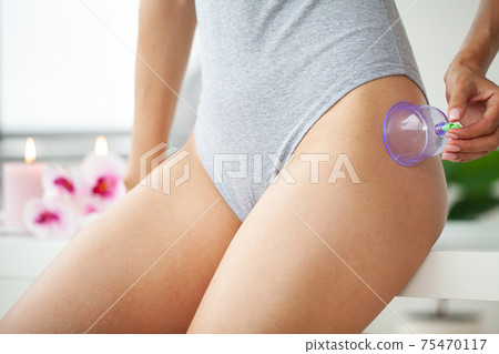Woman getting anti-cellulite massage of hips with use of vacuum cans in beauty studio Woman getting anti-cellulite massage of hips with use of vacuum cans in beauty studio 75470117