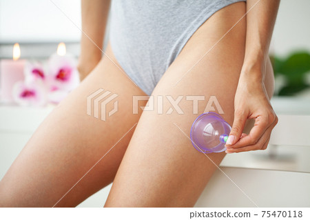 Woman getting anti-cellulite massage of hips with use of vacuum cans in beauty studio Woman getting anti-cellulite massage of hips with use of vacuum cans in beauty studio 75470118