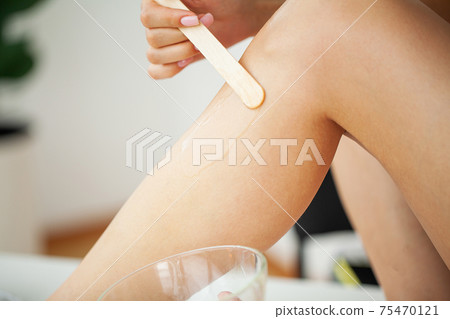Beautician waxing female legs in spa center 75470121