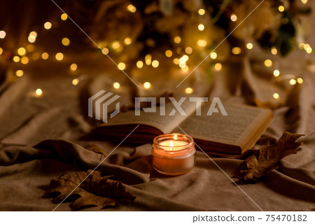 A burning candle on a wooden table in front of a book in a half-mast A burning candle on a wooden table in front of a book in a half-mast 75470182