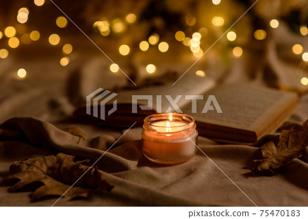 A burning candle on a wooden table in front of a book in a half-mast A burning candle on a wooden table in front of a book in a half-mast 75470183